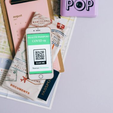 Flat lay of travel essentials with smartphone health passport, camera, map, and documents.